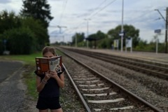 Dzieczynka czyta ksiązkę przy torach, na stacji kolejowej