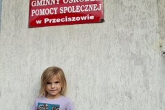 Dziewczynka na tle budynku biblioteki, w rękach trzyma książkę