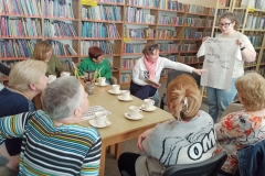 Kobiety przy stole patrzą jak jedna z pań pokazuje koszulkę