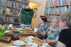 Panie siedzą przy stole,  rozmawiają i oglądają ubrania